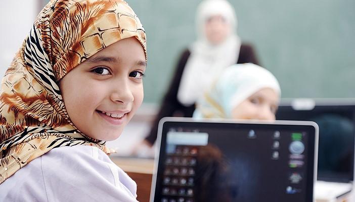 smiling girl wearing a headscarf in a classroom with an open laptop on the desk