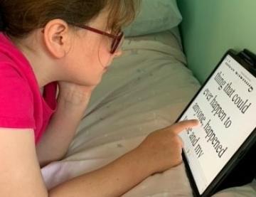 Jessica, a 10 year old girl, lying on her bed, reading on her iPad which is leaning against the wall