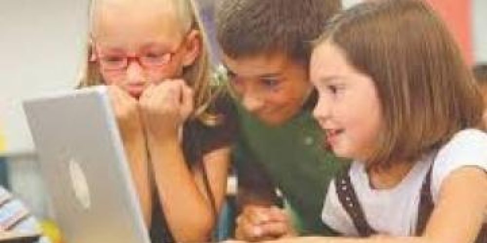 3 young shildren leaning over an open laptop on a desk