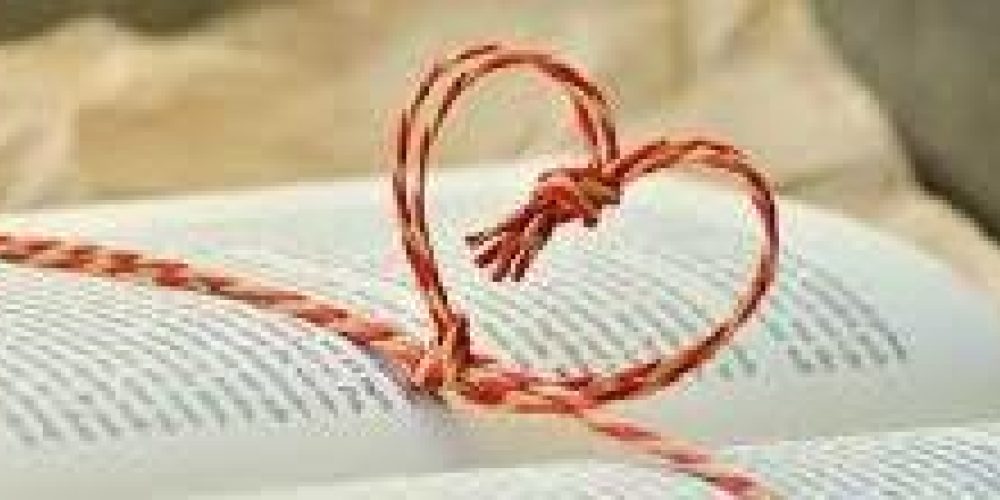 An open book with a piece of red cord twisted into a heart outline across the open pages