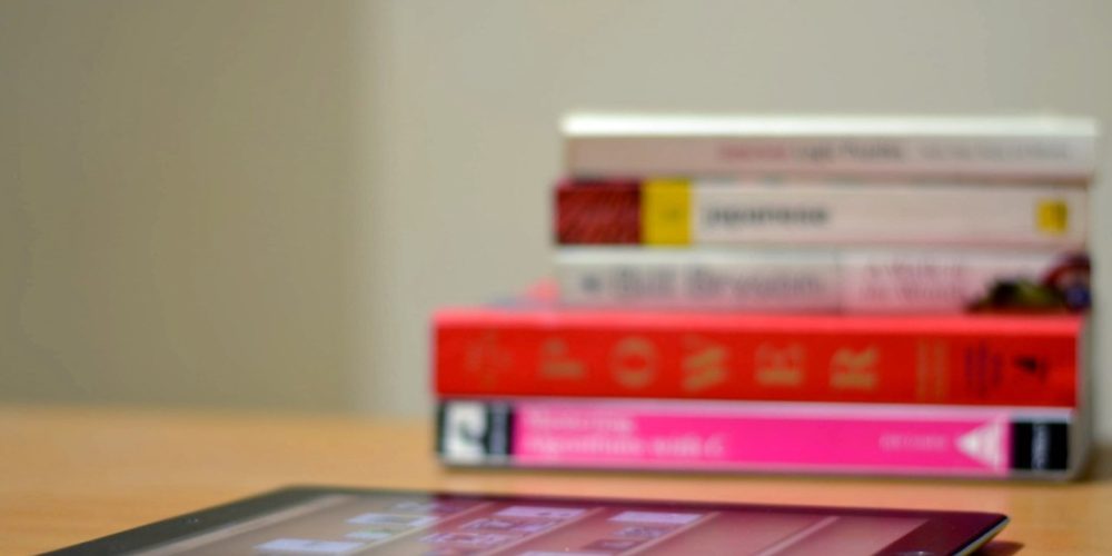 Stack of books on a desk, ipad in front.