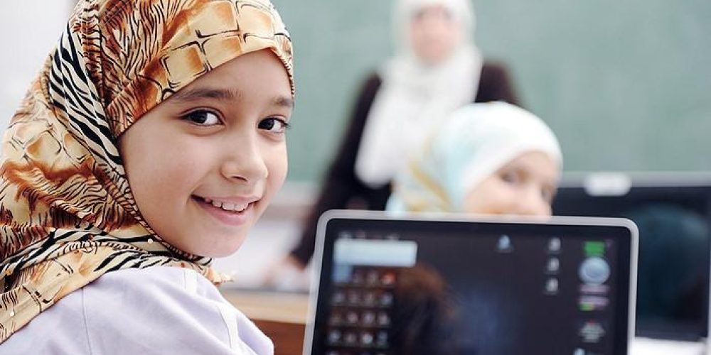 Smiling girl in headress in a classroon an laptop on the desk in front of her