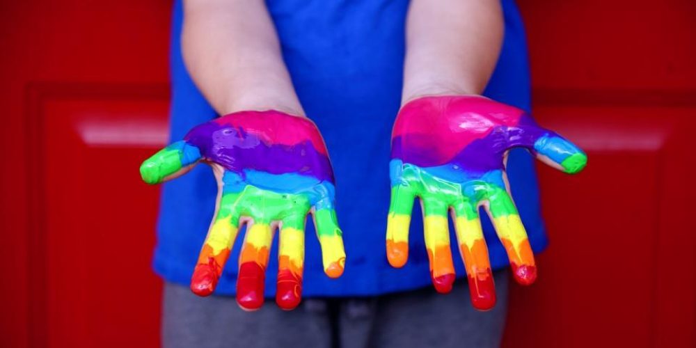 Outstretched child's hands with rainbow coloured paint.