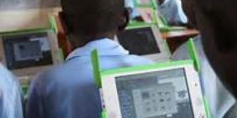 Learner looking at a tablet, facing towards class with other learners sat at desks.