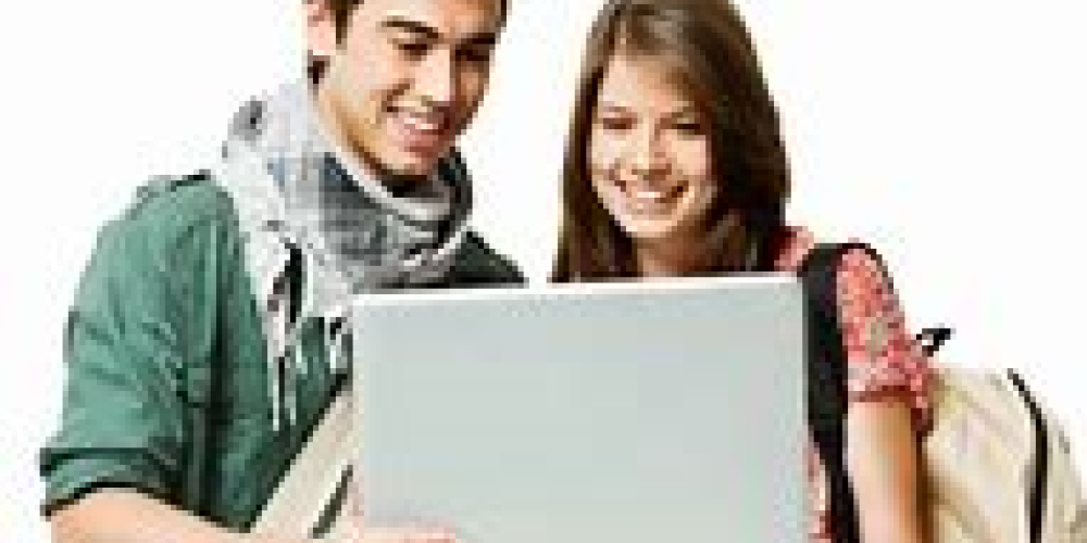 two young adults standing looking at an open laptop together