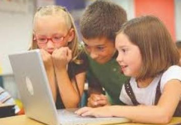 3 young shildren leaning over an open laptop on a desk