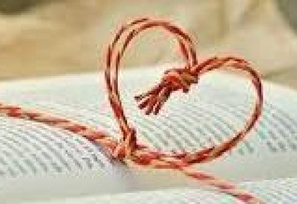 An open book with a piece of red cord twisted into a heart outline across the open pages