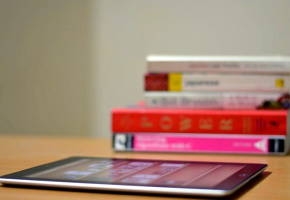 Stack of books on a desk, ipad in front.