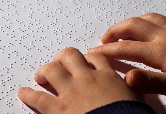 Embossed braille page with hands scanning the page.