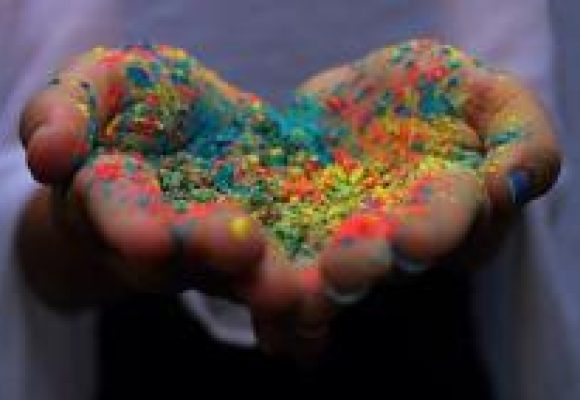 open cupped hands in shape of a heart holding powder in assorted rainbow colours