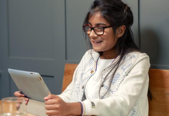 Teenage girl look at iPad in hand, sat in a classroom