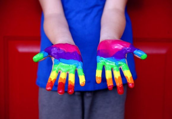 Outstretched child's hands with rainbow coloured paint.