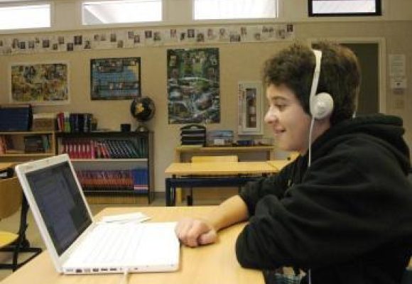 student with headphones , sat at a desk looking at their laptop