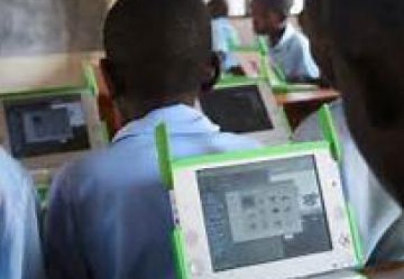 Learner looking at a tablet, facing towards class with other learners sat at desks.