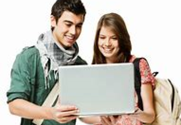 two young adults standing looking at an open laptop together